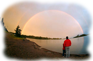 Hombre de rojo de pi&eacute;, de espaldas frente a un lago y un arco iris